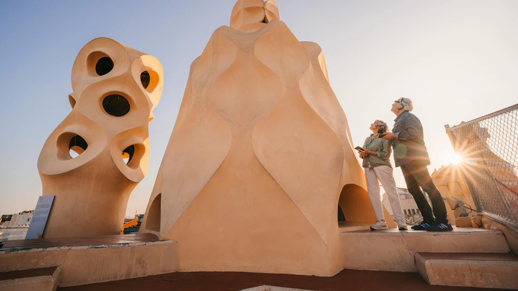 Visitors admire chimneys on La Pedrera rooftop during sunset in Barcelona.