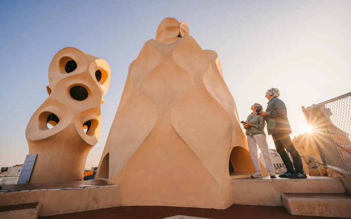 Visitors admire chimneys on La Pedrera rooftop during sunset in Barcelona.