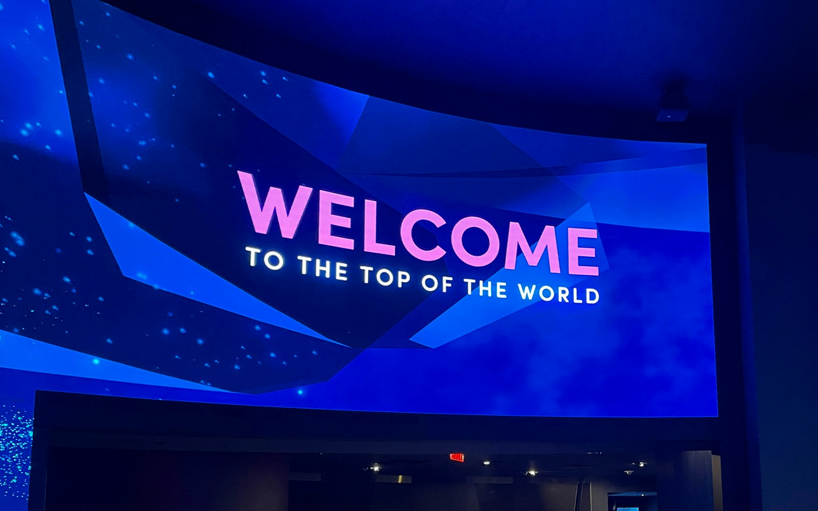 Curved welcome screen at One World Observatory displaying global greetings.