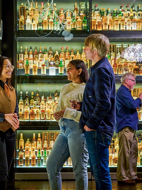 Visitors enjoying The Silver Tour at Scotch Whisky Experience, surrounded by whisky bottles.