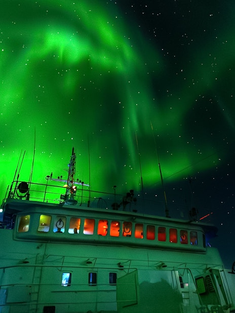 Cruise ship under Northern Lights in Reykjavik night sky.