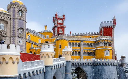 Pena Palace in Sintra with colorful towers and snow falling.
