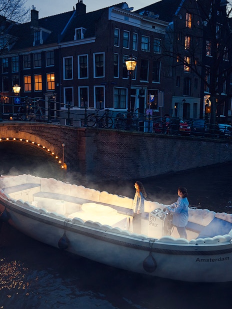 Cloud Boat Cruise on Amsterdam canal at dusk with illuminated bridge.