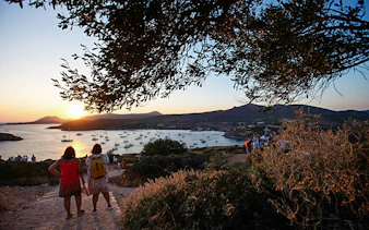 Tourists watching sunset over Cape Sounion with boats in the bay, Greece.