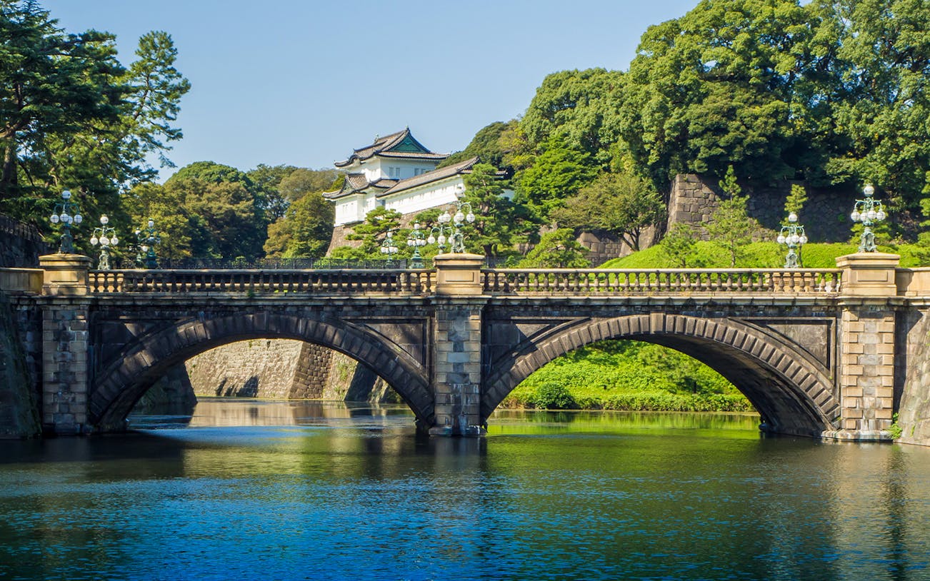 Stone bridge leading to Imperial Palace Tokyo with lush greenery and water.
