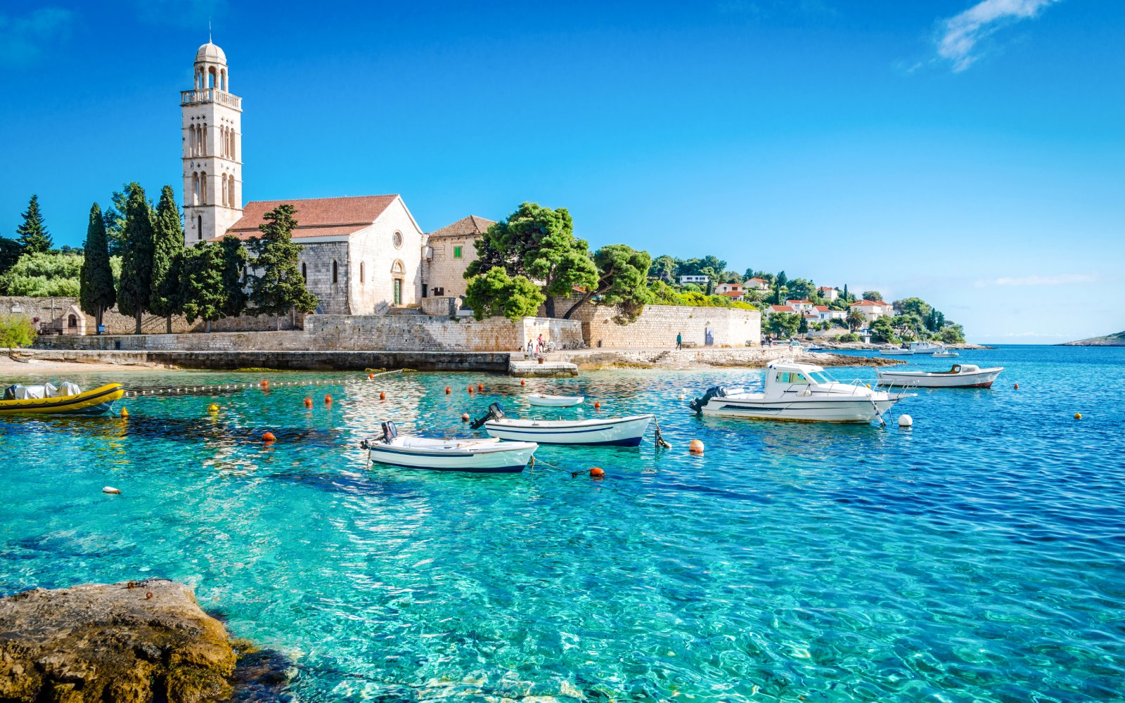 Boats on clear blue water near a historic church on Hvar Island, Croatia.