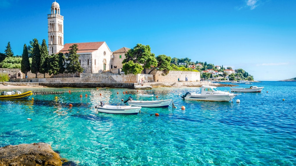Boats on clear blue water near a historic church on Hvar Island, Croatia.