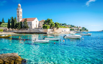 Boats on clear blue water near a historic church on Hvar Island, Croatia.