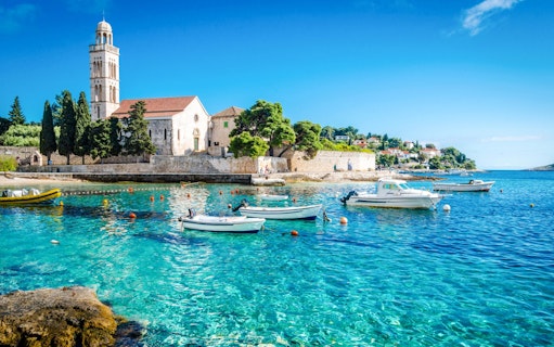 Boats on clear blue water near a historic church on Hvar Island, Croatia.