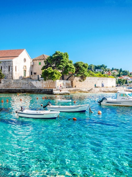 Boats on clear blue water near a historic church on Hvar Island, Croatia.