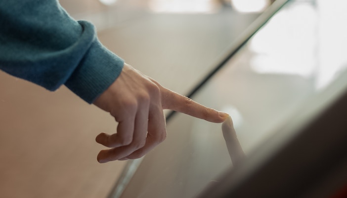 Finger interacting with a digital kiosk screen.
