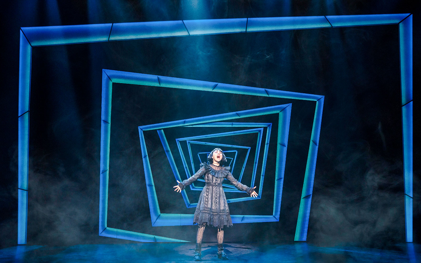 Performer on stage at Beetlejuice Broadway show with geometric backdrop.