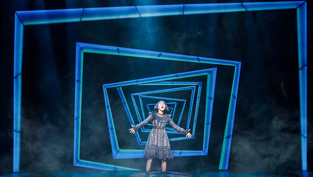 Performer on stage at Beetlejuice Broadway show with geometric backdrop.