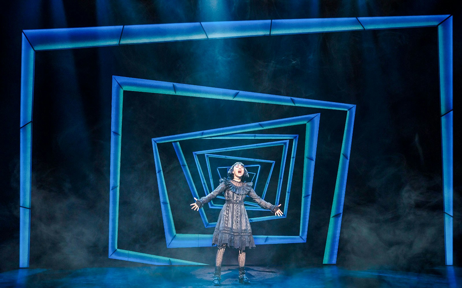 Performer on stage at Beetlejuice Broadway show with geometric backdrop.