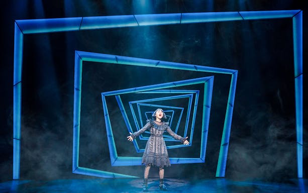 Performer on stage at Beetlejuice Broadway show with geometric backdrop.