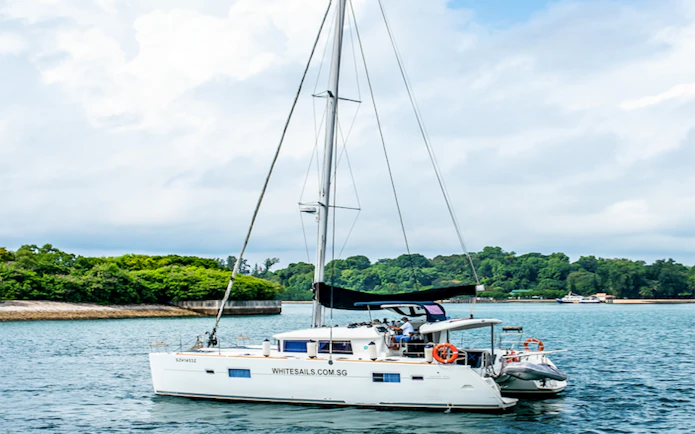 Private yacht SunRise sailing near lush green coastline.