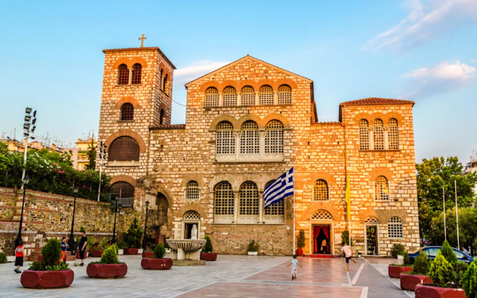 Hagios Demetrios church facade with Greek flag in Thessaloniki, Greece.