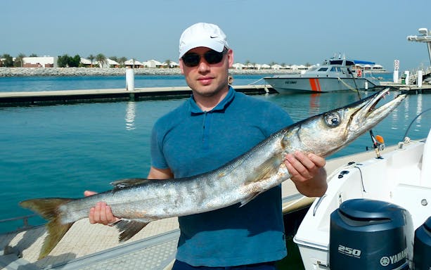 Man holding a large fish on a deep sea fishing charter near a marina.