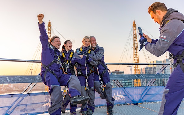 Climbers celebrating atop the O2 Arena roof with London's skyline in view.
