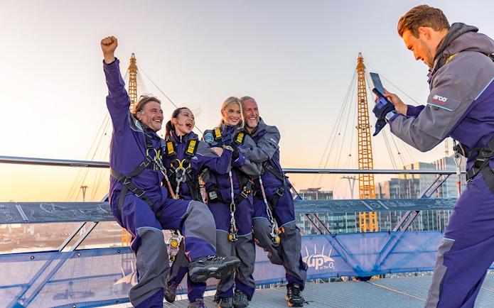 Climbers celebrating atop the O2 Arena roof with London's skyline in view.