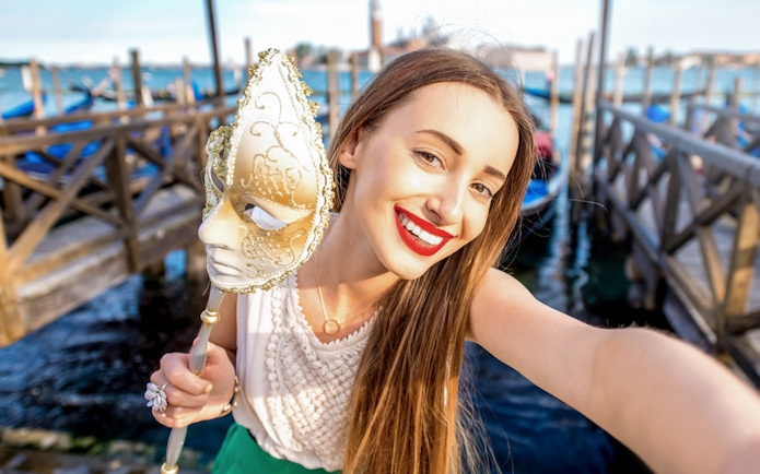 Woman holding a Venetian mask near gondolas on a Venice walking tour.