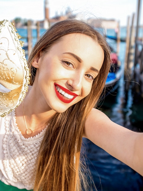 Woman holding a Venetian mask near gondolas on a Venice walking tour.
