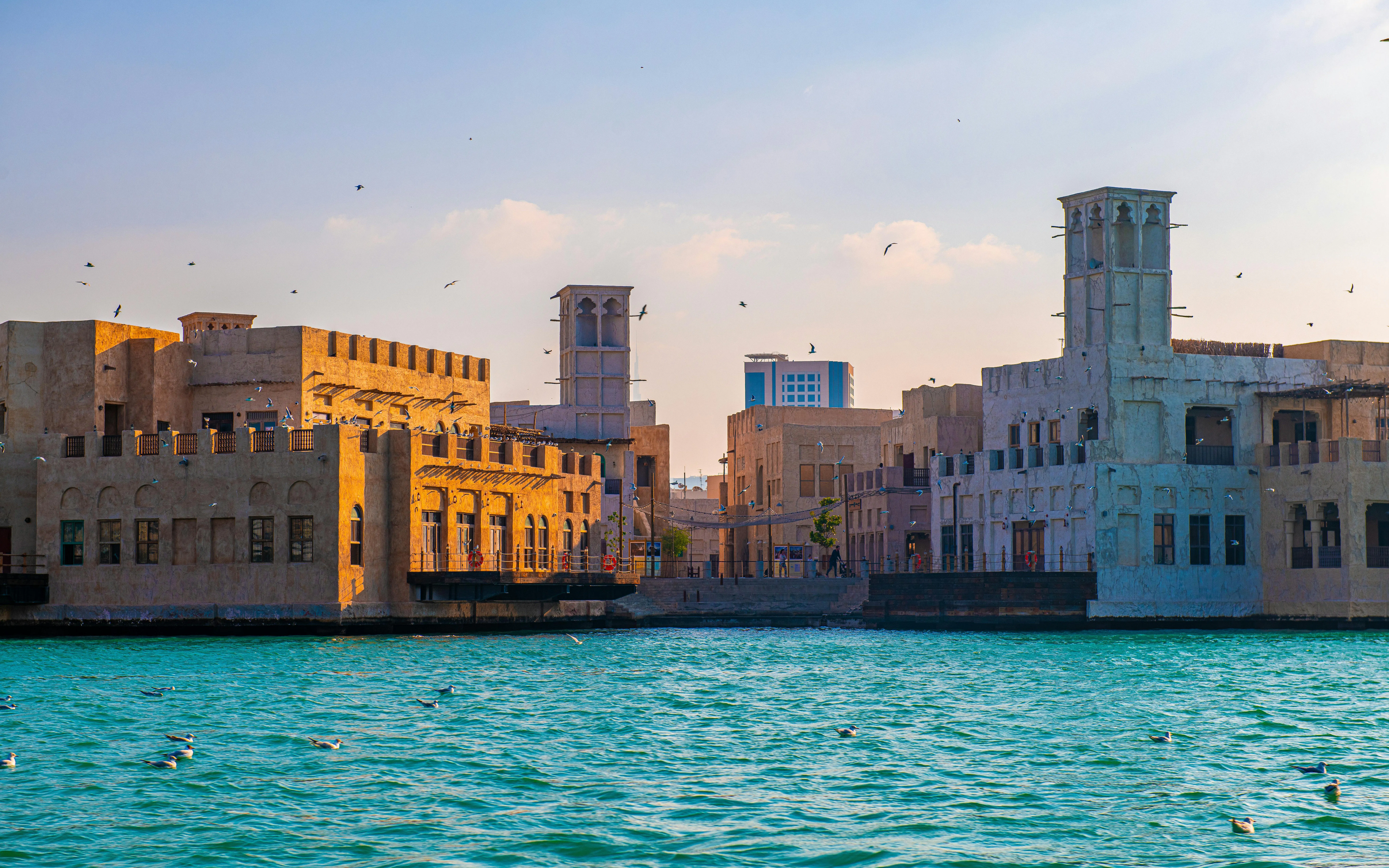 Traditional wind towers along Dubai Creek at sunset.
