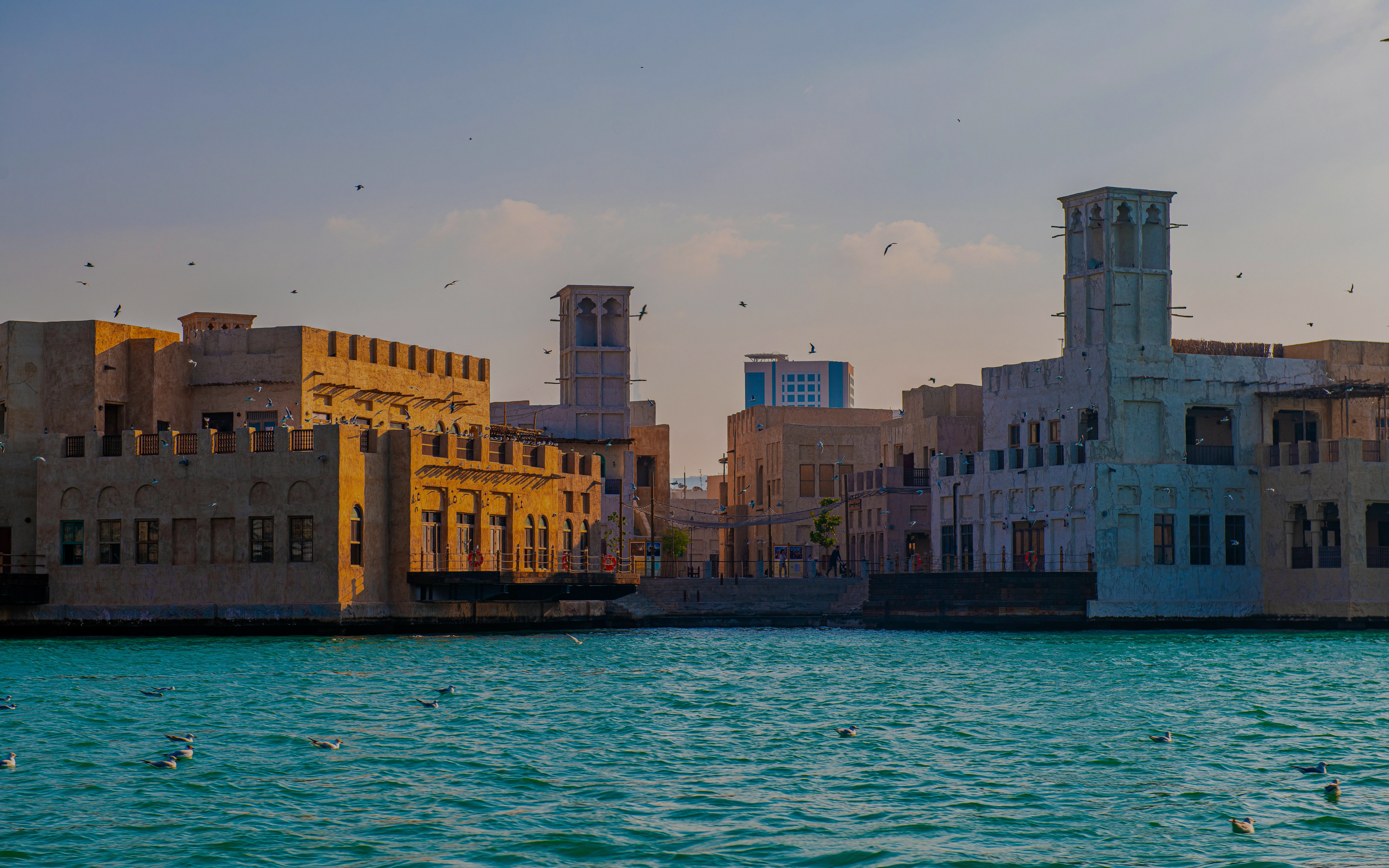 Traditional wind towers along Dubai Creek at sunset.