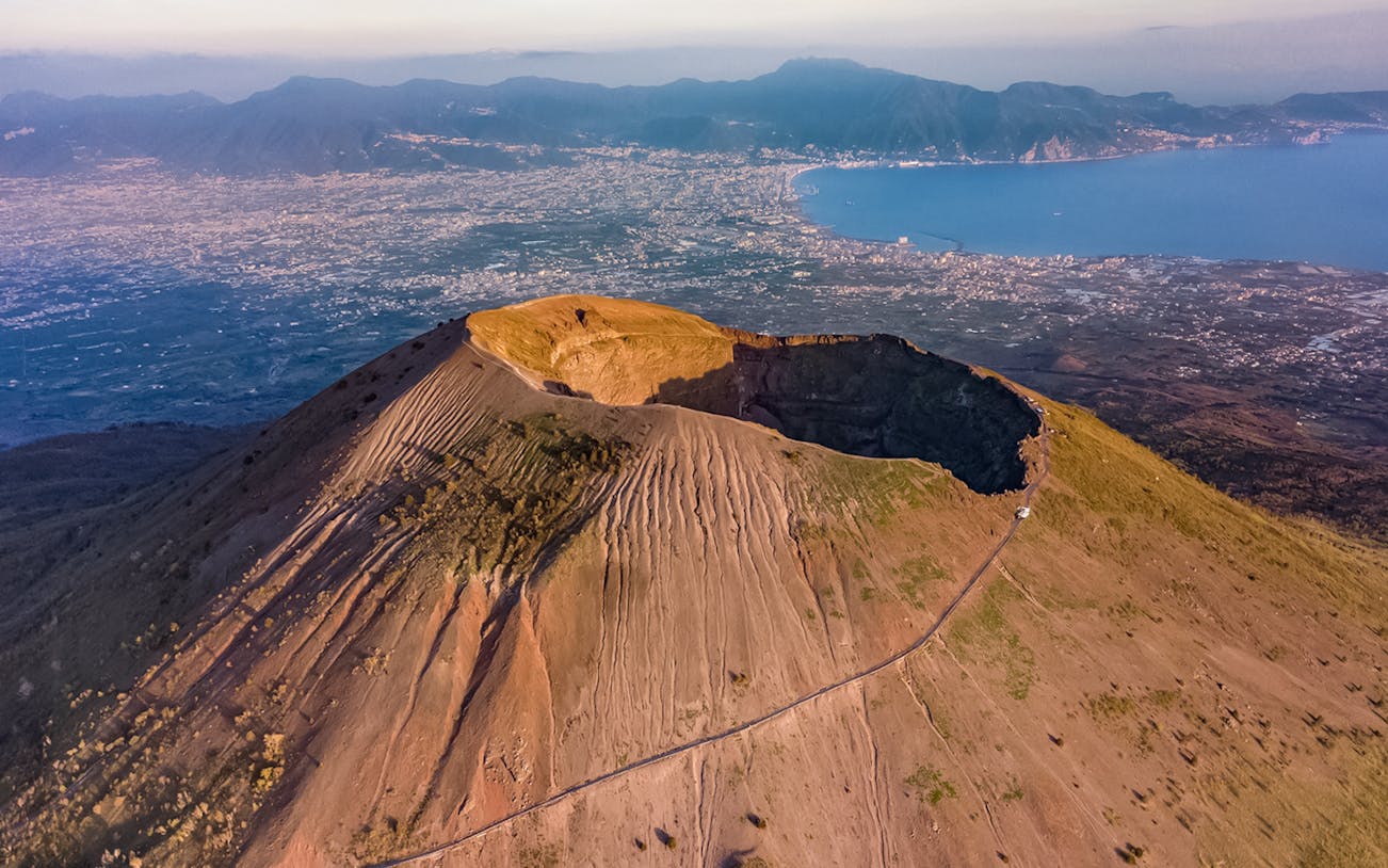 Aerial view of Vesuvius Volcano crater with Naples and coastline in the background.