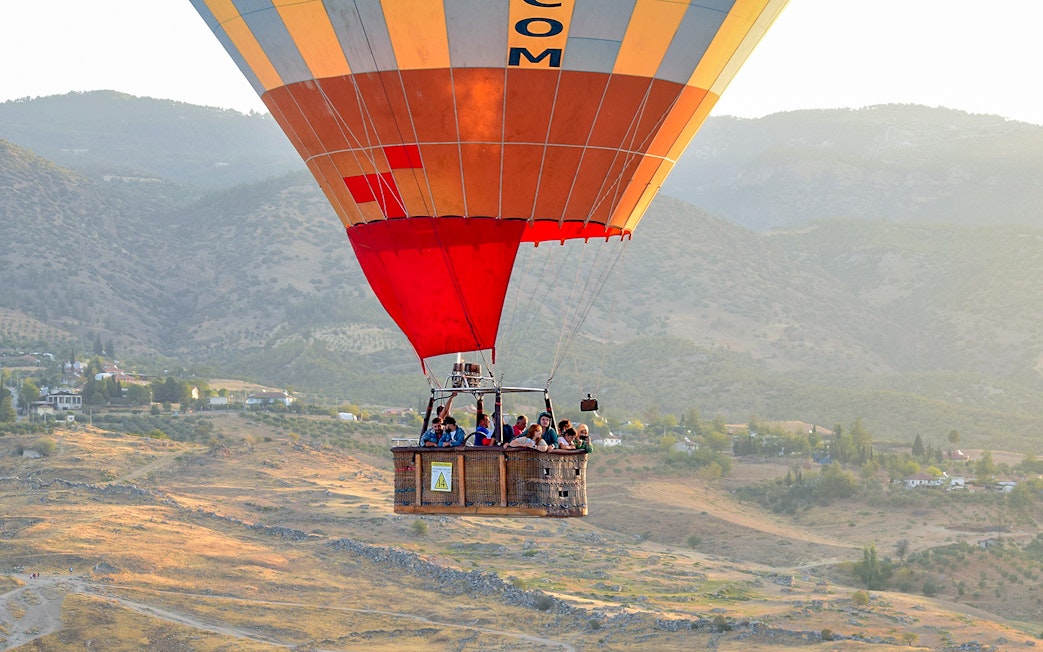 Hot air balloon with passengers over Pamukkale's limestone terraces, Turkey.
