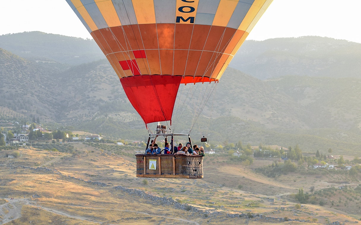 Hot air balloon with passengers over Pamukkale's limestone terraces, Turkey.