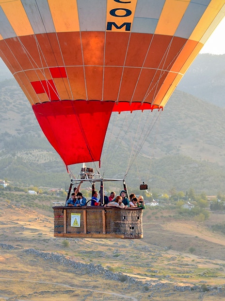 Hot air balloon with passengers over Pamukkale's limestone terraces, Turkey.