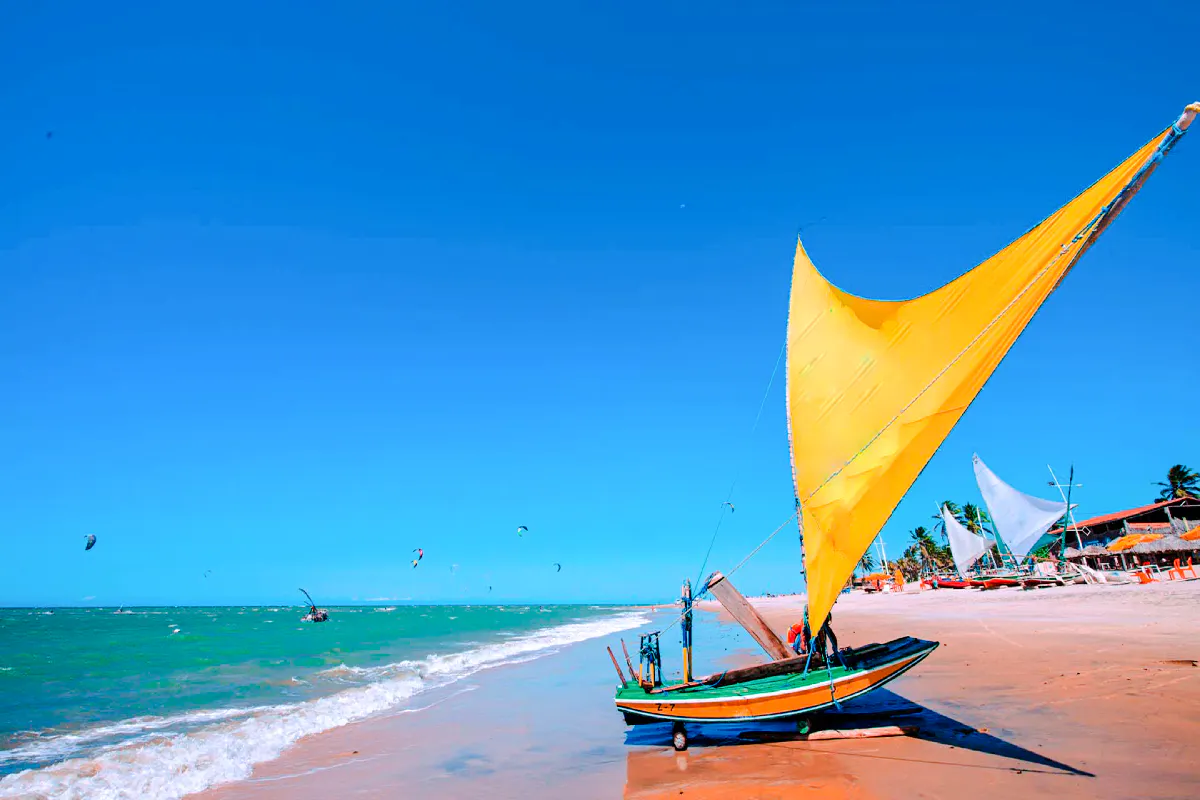 Traditional jangada boat on Cumbuco beach with kitesurfers in the ocean, Sao Paulo tour.