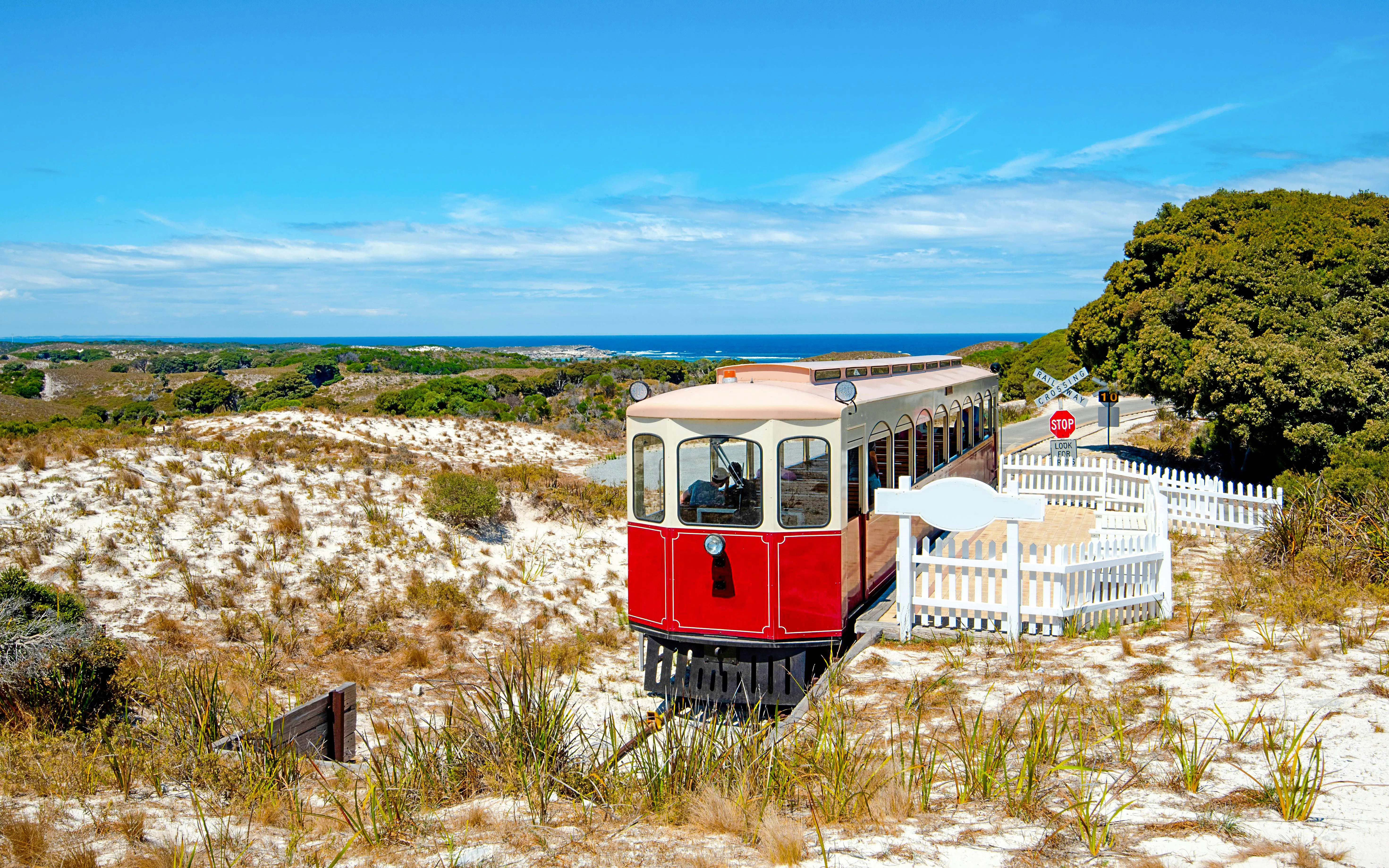 Red train on Oliver Hill Railway, Rottnest Island, Australia, with coastal landscape in background.