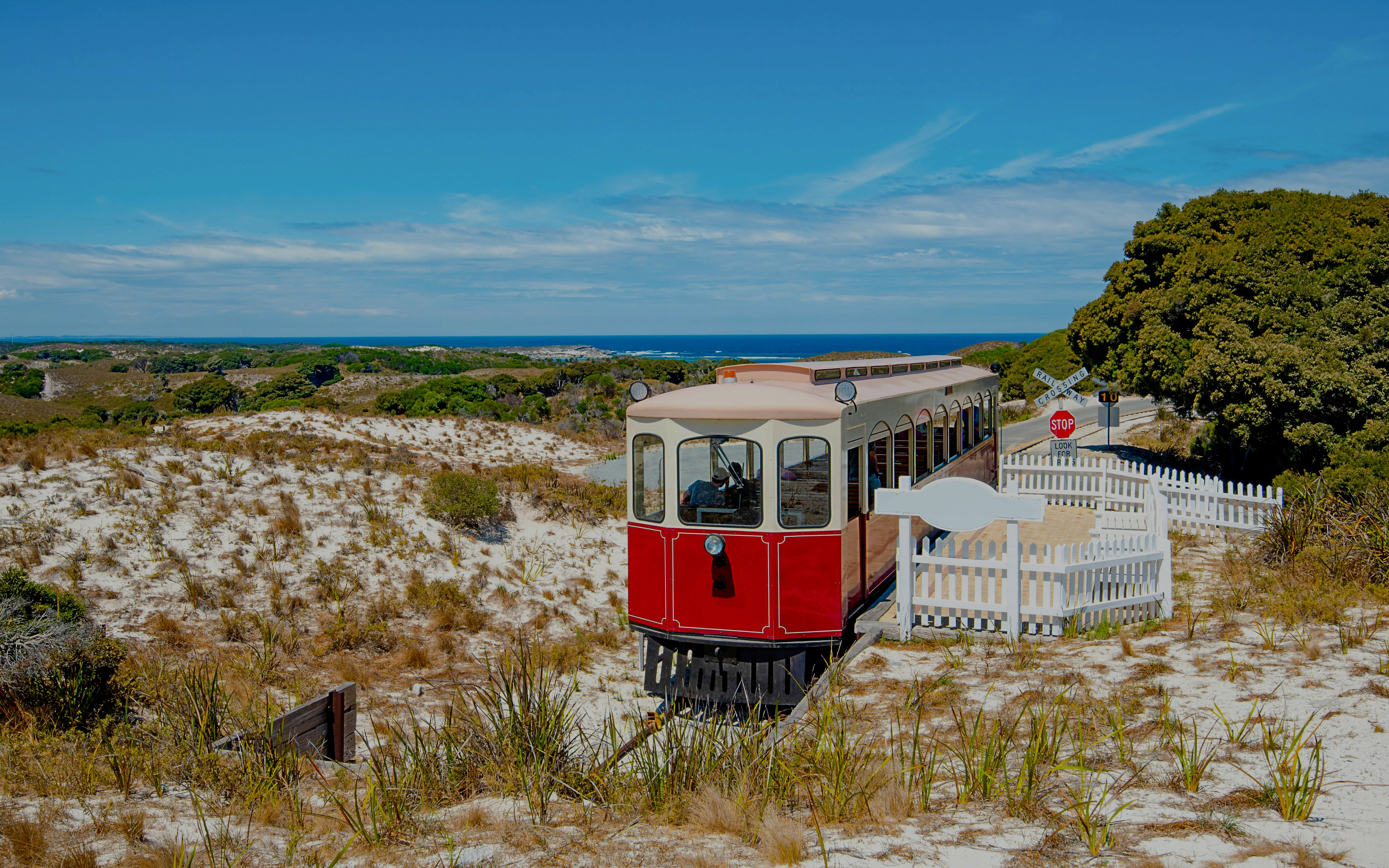 Red train on Oliver Hill Railway, Rottnest Island, Australia, with coastal landscape in background.