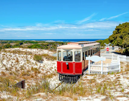 Red train on Oliver Hill Railway, Rottnest Island, Australia, with coastal landscape in background.