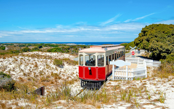 Red train on Oliver Hill Railway, Rottnest Island, Australia, with coastal landscape in background.