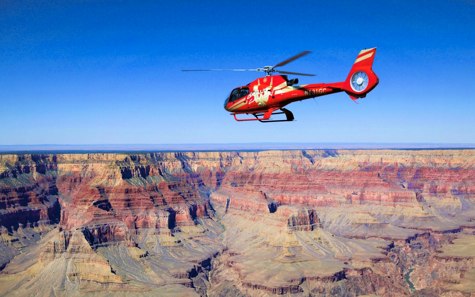 Helicopter flying over the Grand Canyon, showcasing vast rock formations and Colorado River below.
