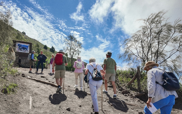 Hikers ascending Mount Vesuvius trail under a clear sky.