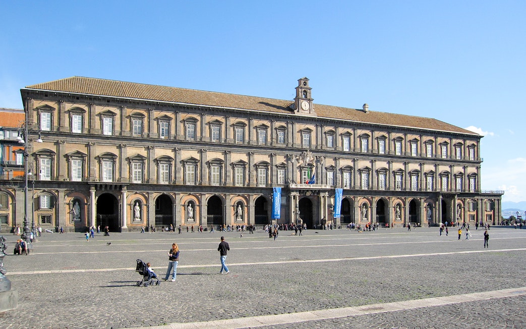 Royal Palace of Naples facade with visitors in the courtyard.