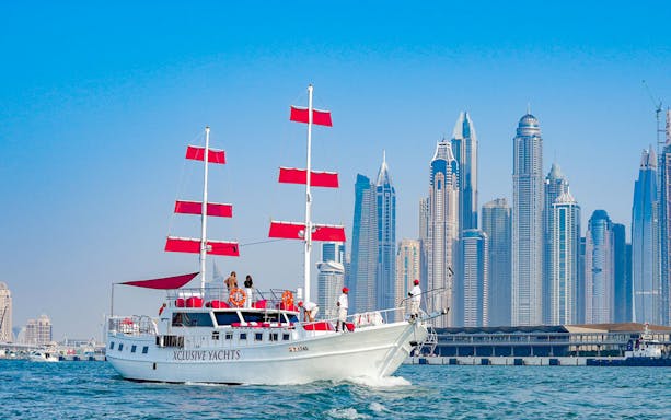 Sailing yacht with red sails in Dubai Marina, skyscrapers in the background.