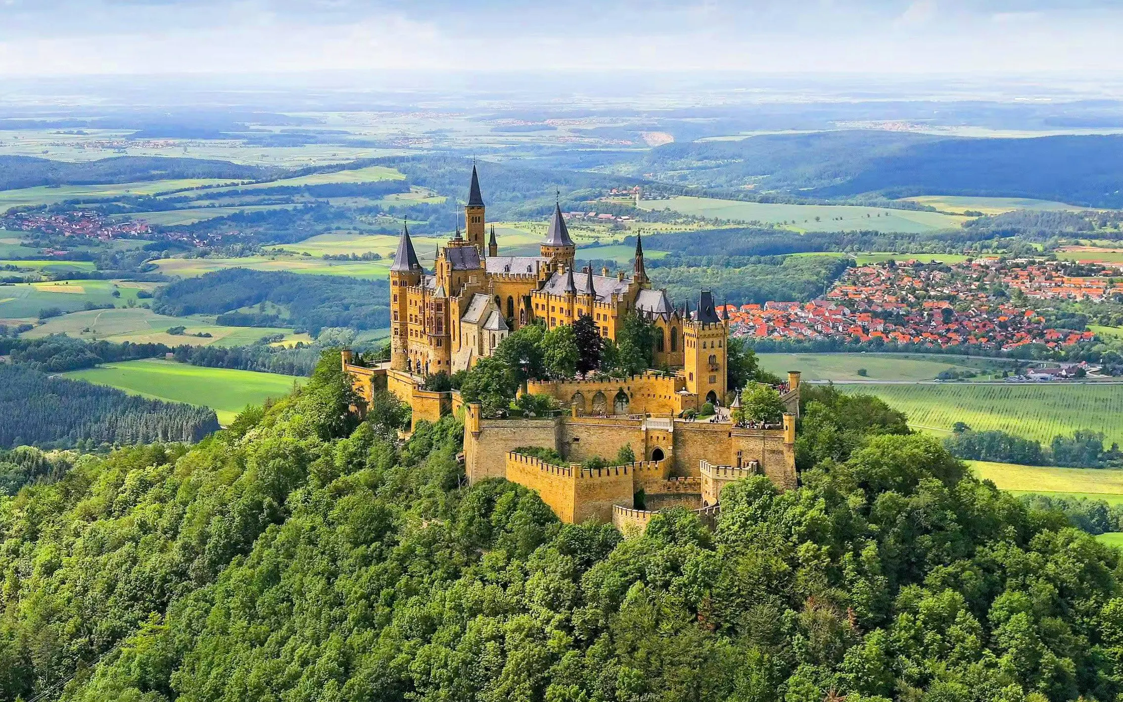 Hohenzollern Castle atop a forested hill in Germany with surrounding countryside.