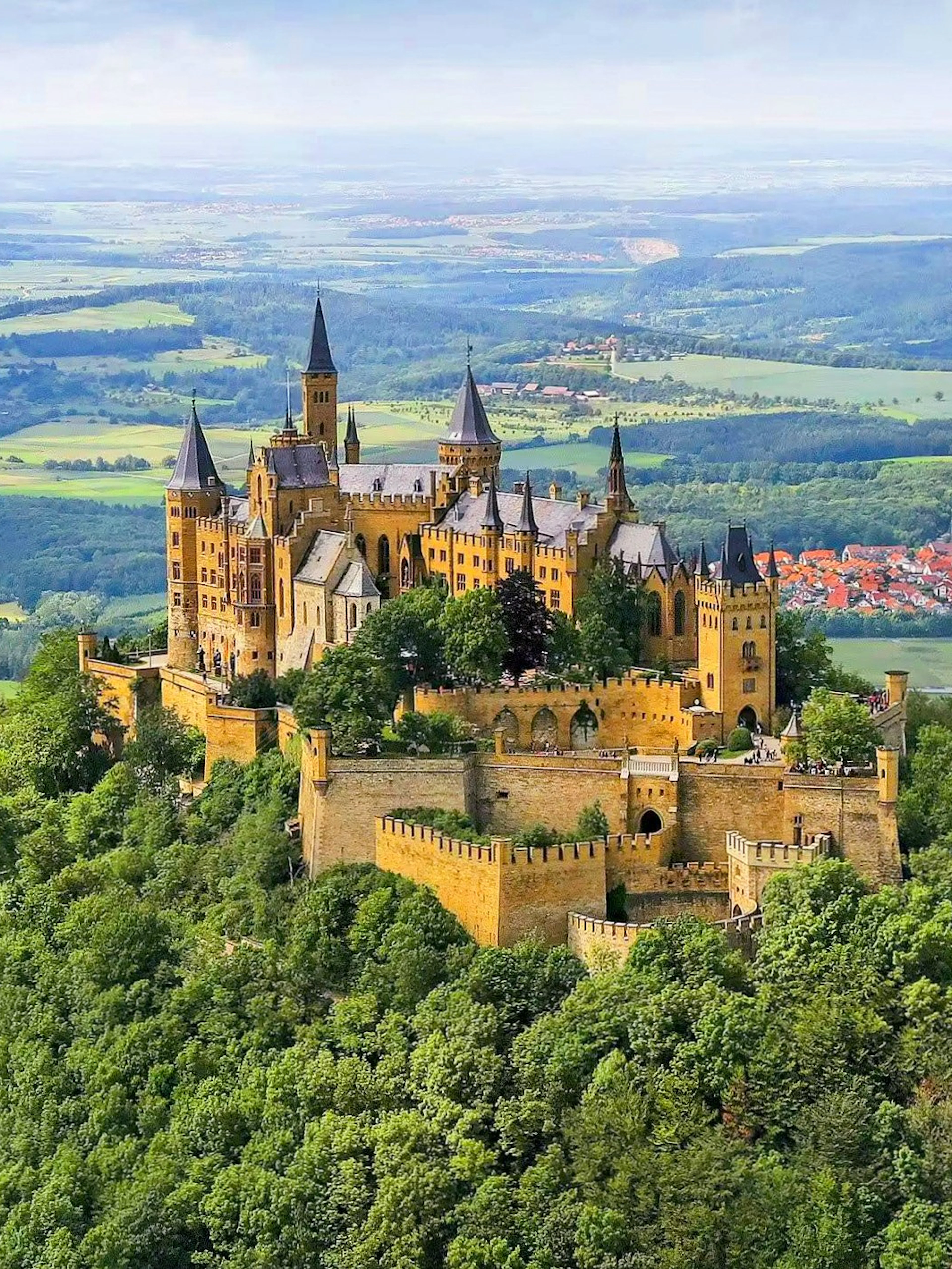 Hohenzollern Castle atop a forested hill in Germany with surrounding countryside.