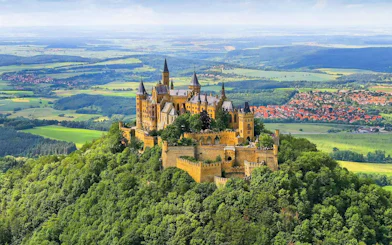 Hohenzollern Castle atop a forested hill in Germany with surrounding countryside.