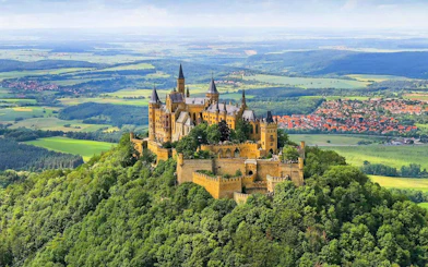 Hohenzollern Castle atop a forested hill in Germany with surrounding countryside.