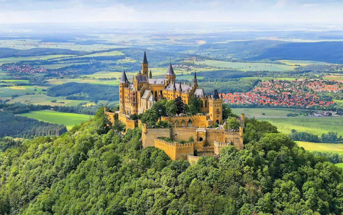Hohenzollern Castle atop a forested hill in Germany with surrounding countryside.