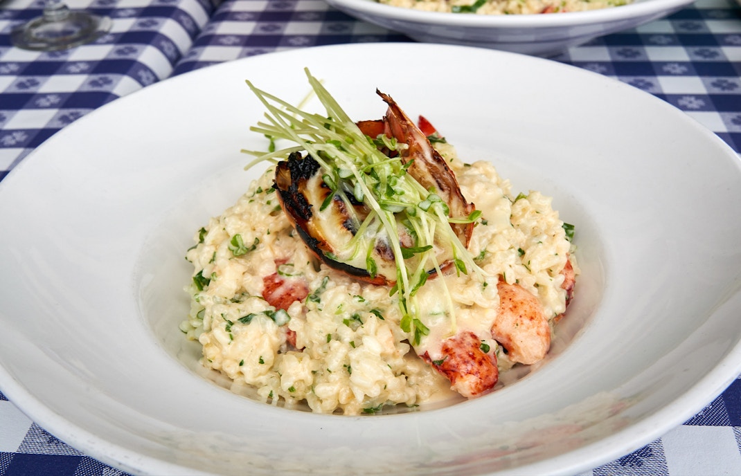 Lobster risotto garnished with greens on a white plate.