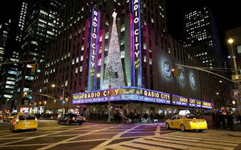 Radio City Music Hall at night, New York City, with taxis and holiday lights.