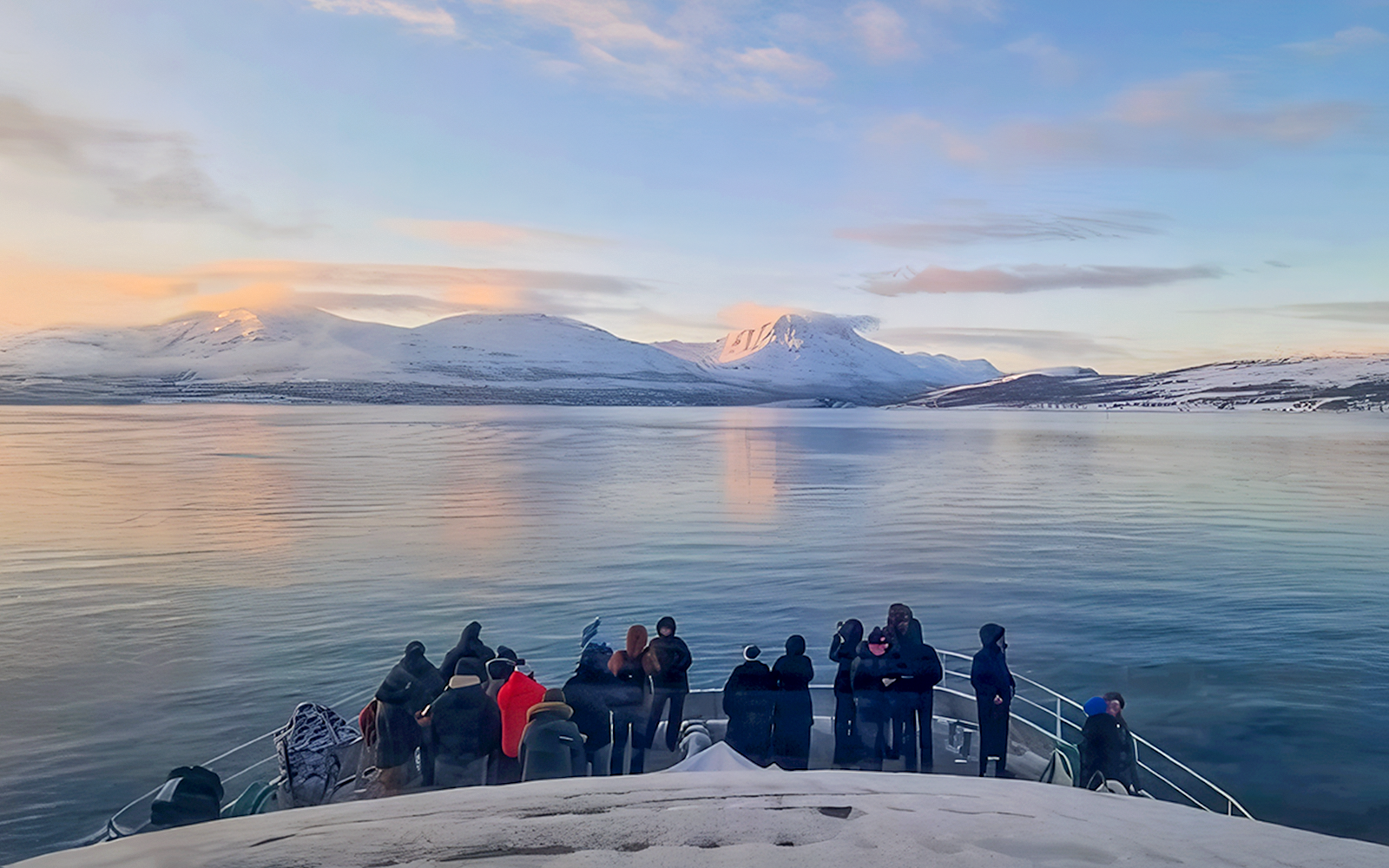 Guests on a boat watching for whales in Tromso with snowy mountains in the background.