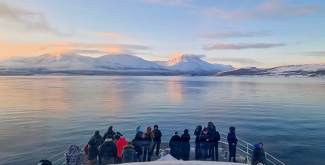 Guests on a boat watching for whales in Tromso with snowy mountains in the background.